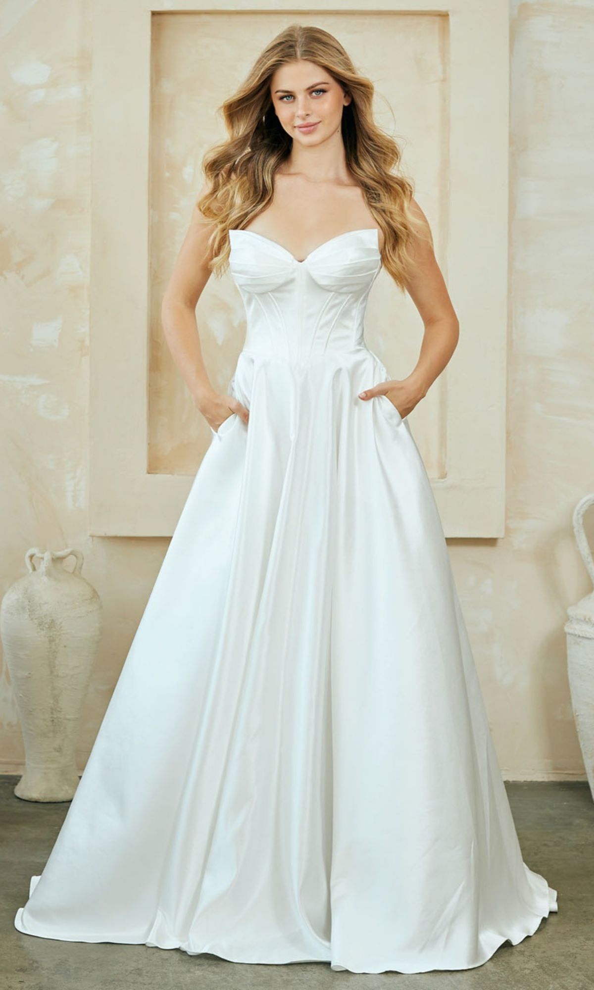 Woman wearing a strapless long white dress with her hands in the a-line skirt's pockets, standing indoors.